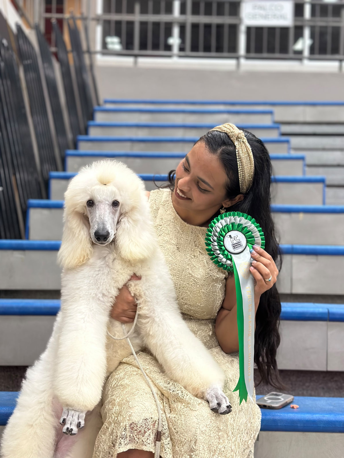 Adaia sentada en las gradas con un caniche blanco y una escarapela verde de exposición