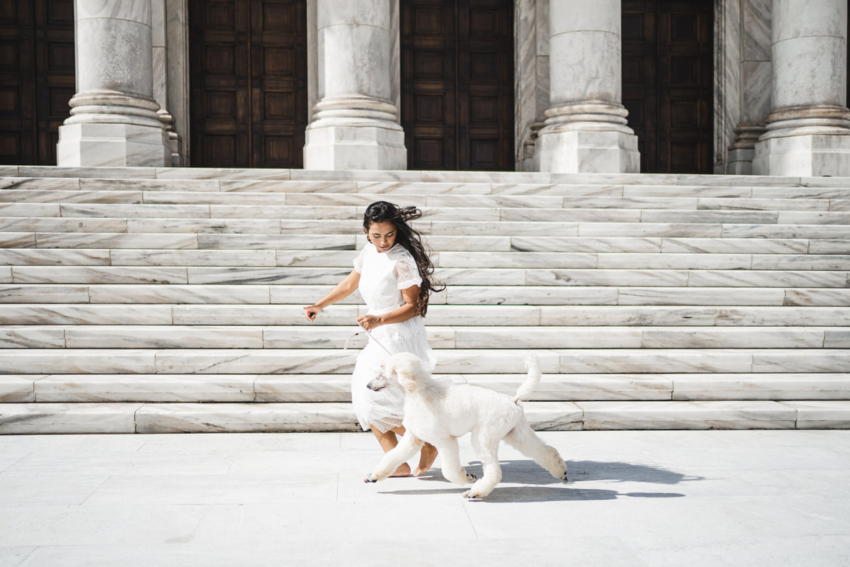 Adaia descalza, con vestido blanco, trota con un caniche blanco frente a una escalinata de mármol