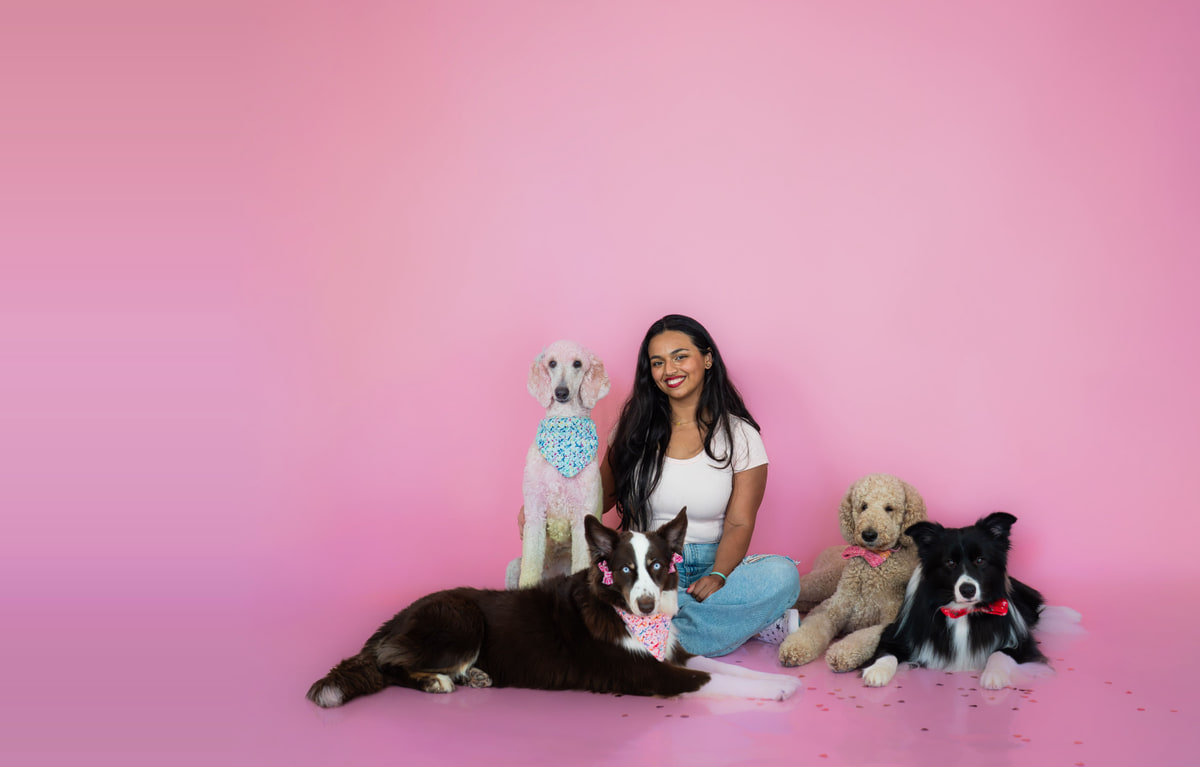 Adaia sonriendo con cuatro perros sobre un fondo rosado